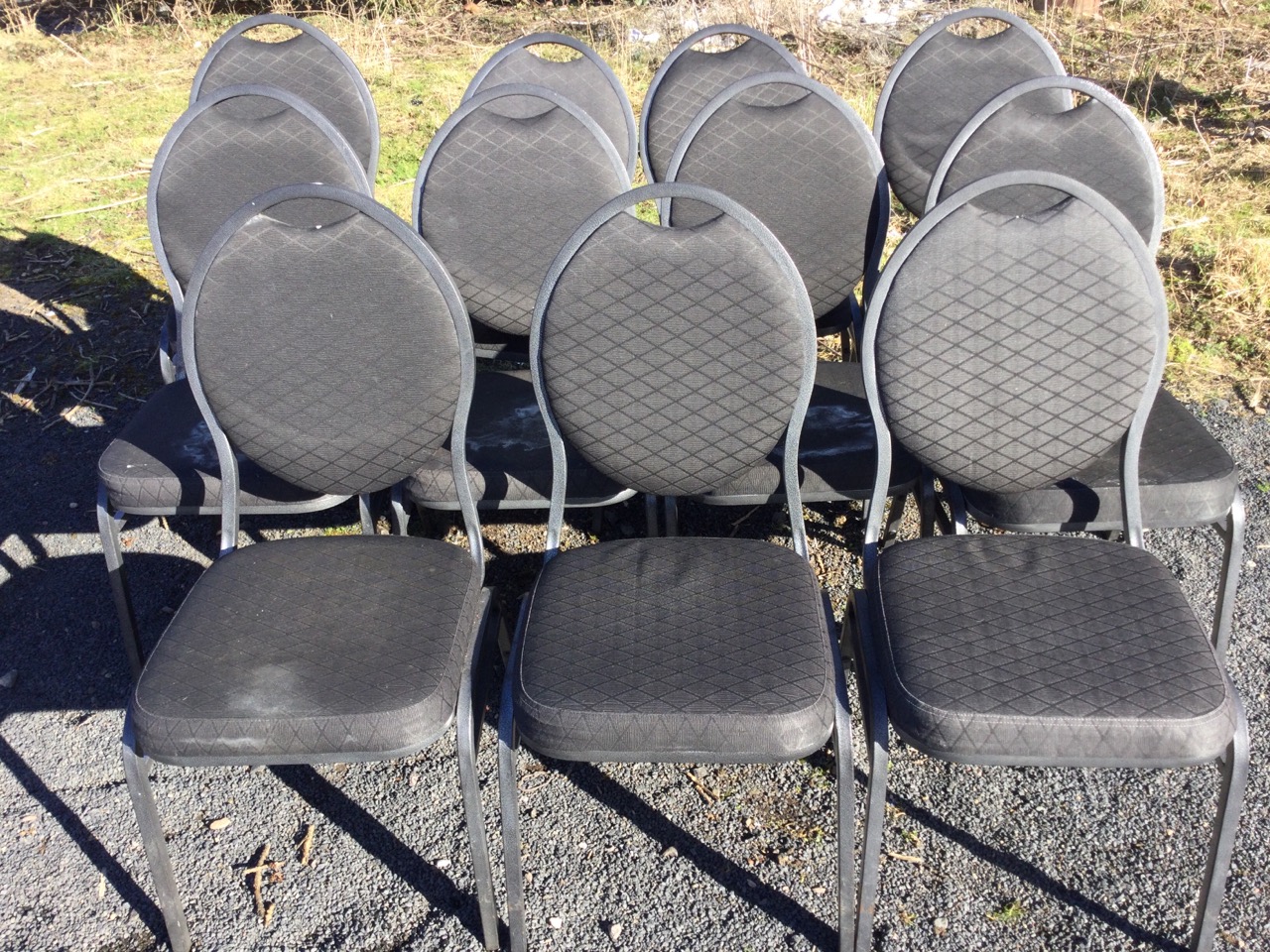 A set of eleven stacking chairs with oval padded backs and cushion seats, raised on square angled