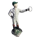 A painted composition stone figure of a young jockey holding ring, standing on square plinth. (44.