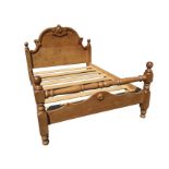 A pine double bed, with carved arched headboard framed by square cornerposts with ball finials,