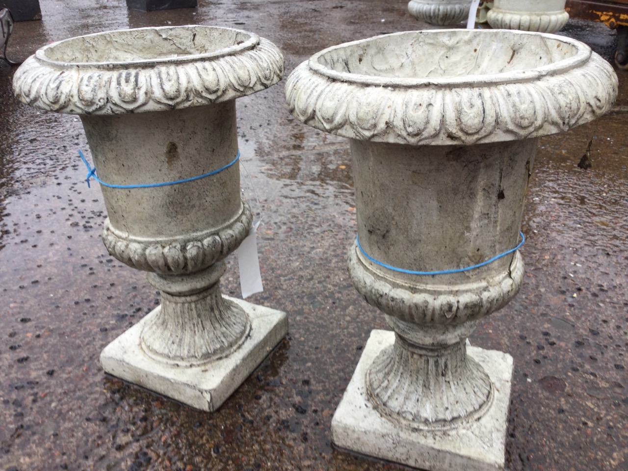 A pair of composition resin garden urns with lozenge moulded rims on fluted tapering bodies, with