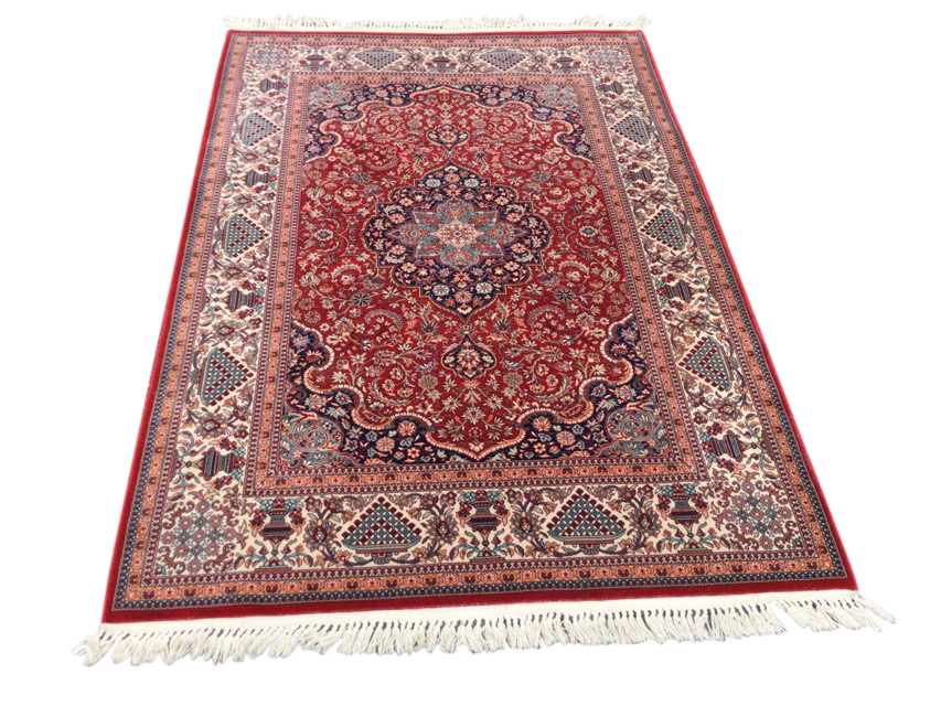 An Indian rug woven with busy red floral field framing a central scalloped blue floral medallion