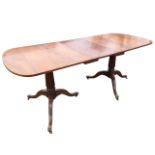 A Georgian style twin pedestal mahogany dining table, the crossbanded top with spare leaf, raised on