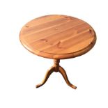 A circular pine lamp table, the moulded top on turned column with tripartite scrolled legs. (24in