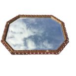 An octagonal mirror with bevelled plate in rectangular pierced scrolled gilt & gesso frame, with