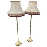 A pair of brass standard lamps with fringed damask shades on columns, raised on octagonal moulded