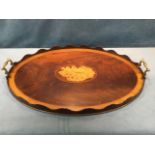 An oval Edwardian crossbanded mahogany tray inlaid with central shell paterae, having waved rim