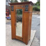 An arts & crafts oak wardrobe with angled cornice above a central bevelled mirror door having