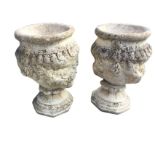 A pair of composition stone urns with moulded rims above bodies embossed with flowers, raised on
