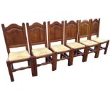 A set of six hardwood dining chairs with arched fielded panelled backs above drop-in rush seats,