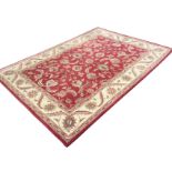 A contemporary oriental style rug woven with red field of linked foliage framed by ivory frieze of