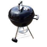 A black Weber BBQ stand with lid and green soft cover, on angle legs with casters.