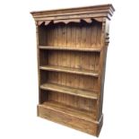 A heavy pine bookcase with moulded cornice above a shaped apron and four thick open shelves, with
