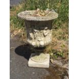 A composition stone urn with lozenge moulded rim having body of classical figures on fluted sockle