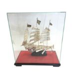A glass cased Chinese silver three-masted junk modelled with oars, anchors, flags, canons and