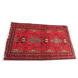 An Indian rug woven in an aztec style with two central serrated leaf medallions on red field