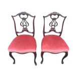 A pair of late Victorian mahogany saloon chairs with pierced scroll carved backs above stuffover