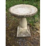 A composition stone birdbath, the circular bowl with moulded rim on baluster column above a square
