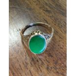 A Victorian gold ring with pierced scrolled apron around an oval bead framed jade panel - struck