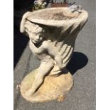 A composition stone birdbath with oval conch shell basin supported by cherub, raised on oval plinth.