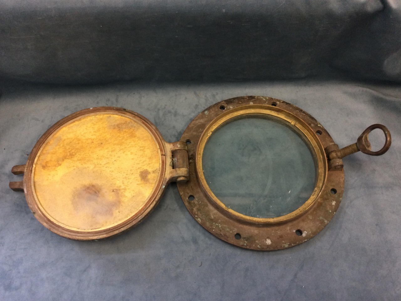 A heavy bronze ships porthole with intact lense, having hinged cover and screw closure, salvaged