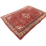 An oriental rug woven with red field of floral grid design around a central serrated lozenge