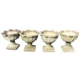 A set of four composition stone urns with circular leaf moulded bowls on waisted supports with