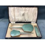 A cased three-piece ladies silver dresssing table set with pale blue/green guilloche enamelling to