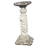 A composition stone birdbath with fluted cast column entwined with mice and ivy leaves beneath a