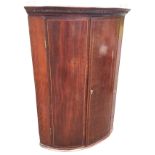 A nineteenth century bowfronted mahogany corner cabinet, with moulded dentil cornice above boxwood