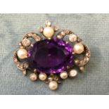An oval Victorian amethyst brooch with cut claw set stone framed by scrolled borders set with pearls