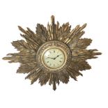 A C20th sunburst type clock with gesso moulded flared frame around a circular brass bezel with roman