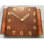 An art deco oak clock with stylised brass numerals & pierced hands, the square dial flanked by