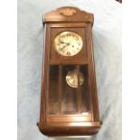 An oak cased 1930s wallclock, the scalloped hood with applied floral decoration above a door flanked