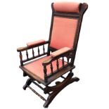 An American mahogany rocking chair with brass studded upholstery, the carved back with headrest,