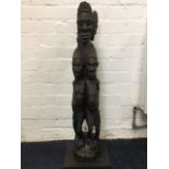 A carved African tribal piece formed from one log, the front with two women beneath bust head with