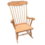 A modern beech rocking chair with shaped back rail on spindles above a laminated seat, raised on