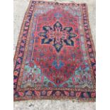An antique oriental rug woven with central deep blue star medallion on red floral field within