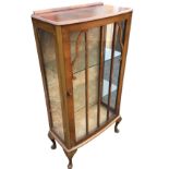 A bowfronted walnut display cabinet with astragal glazed door enclosing glass shelves, with glass