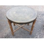 A circular brass topped coffee table, the tray embossed with Islamic decoration having woven type