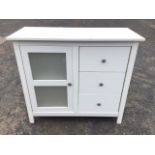 A contemporary white melamine cabinet with rectangular top above three drawers flanking a glazed