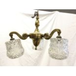 A brass hanging light with column beneath ring above a bun supporting three scrolled branches hung