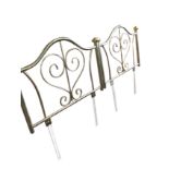 A pair of modern brass headboards with tubular arched rails framing scrolled panels, the cornerposts