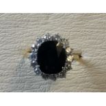 A large sapphire and diamond cluster ring, the oval cut dark sapphire of 4.7 carats framed by a