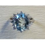 An 18ct white gold aquamarine and diamond cluster ring, the oval cut pale claw set aquamarine