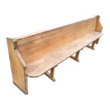 A long Victorian pine pew, the back with tubular rail and hymn book shelf, the plank seat framed