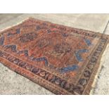 An antique bokarra rug woven with three blue floral medallions on busy madder field with serrated