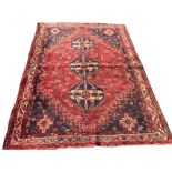 An oriental bokarra rug woven with three linked serrated blue medallions on red field with floral