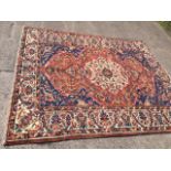 An oriental Indian carpet woven with central ivory backed oval floral medallion in madder field with