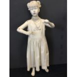 A young girl manikin with articulated arms, wearing embroidered pleated dress with faux pearls. (