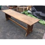A long oak refectory table with four plank top on shaped trestle style supports joined by